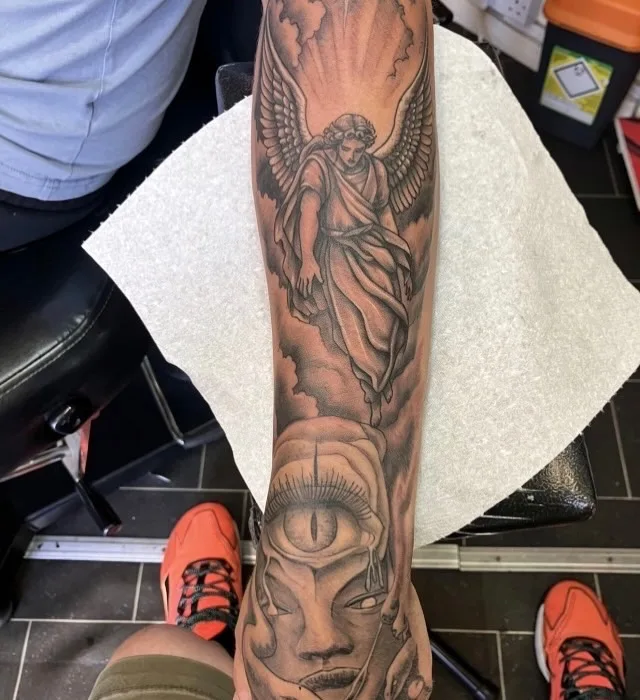 Black and grey archangel forearm sleeve tattoo with clouds, light rays and a spiritual third-eye face, fine shading by Ivan Todorov at N9 Tattoo, Edmonton, North London