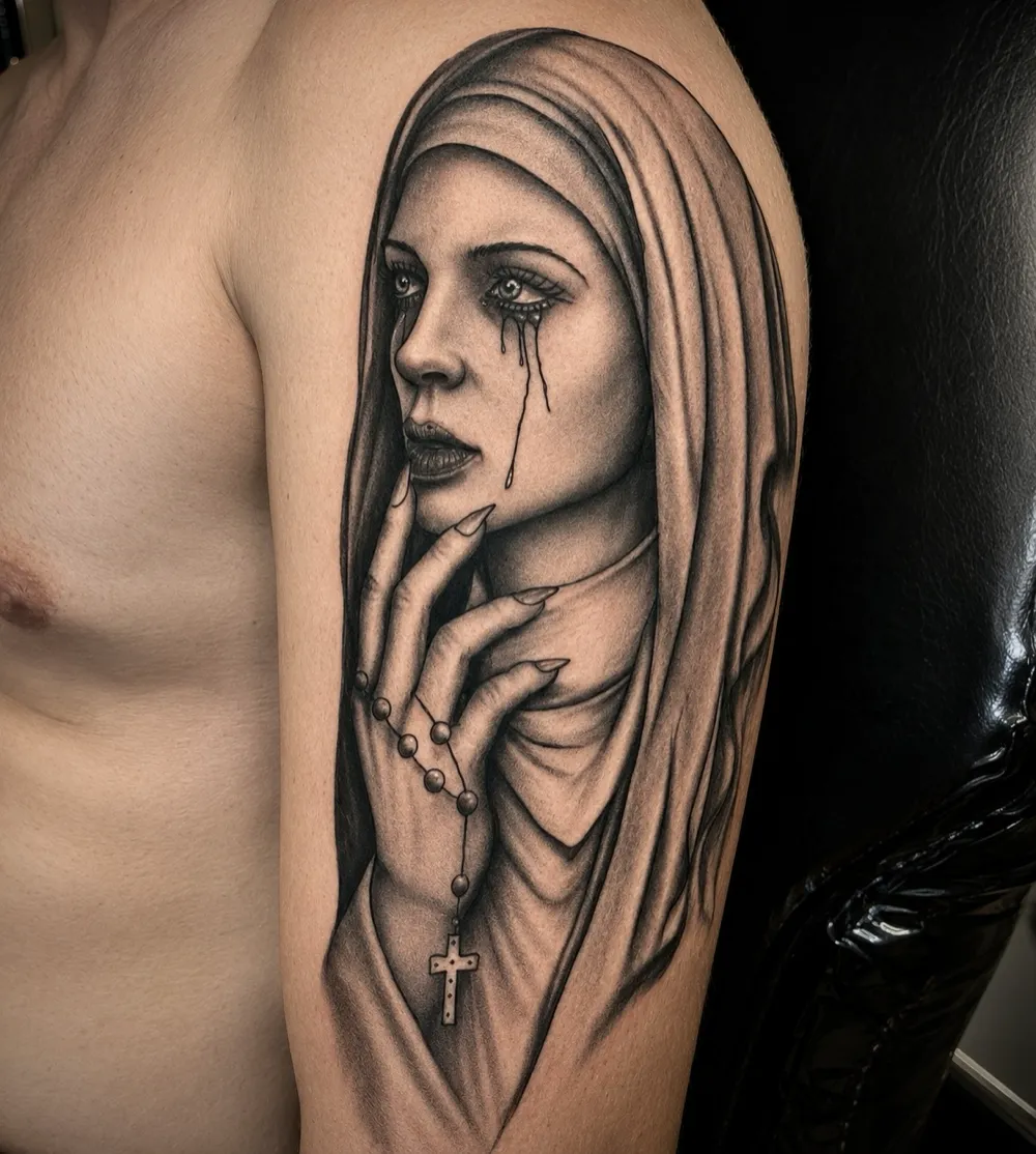Black and grey tattoo of a weeping nun in a veil holding a rosary cross, fine shading upper arm piece by Ivan Todorov at N9 Tattoo, Edmonton, North London